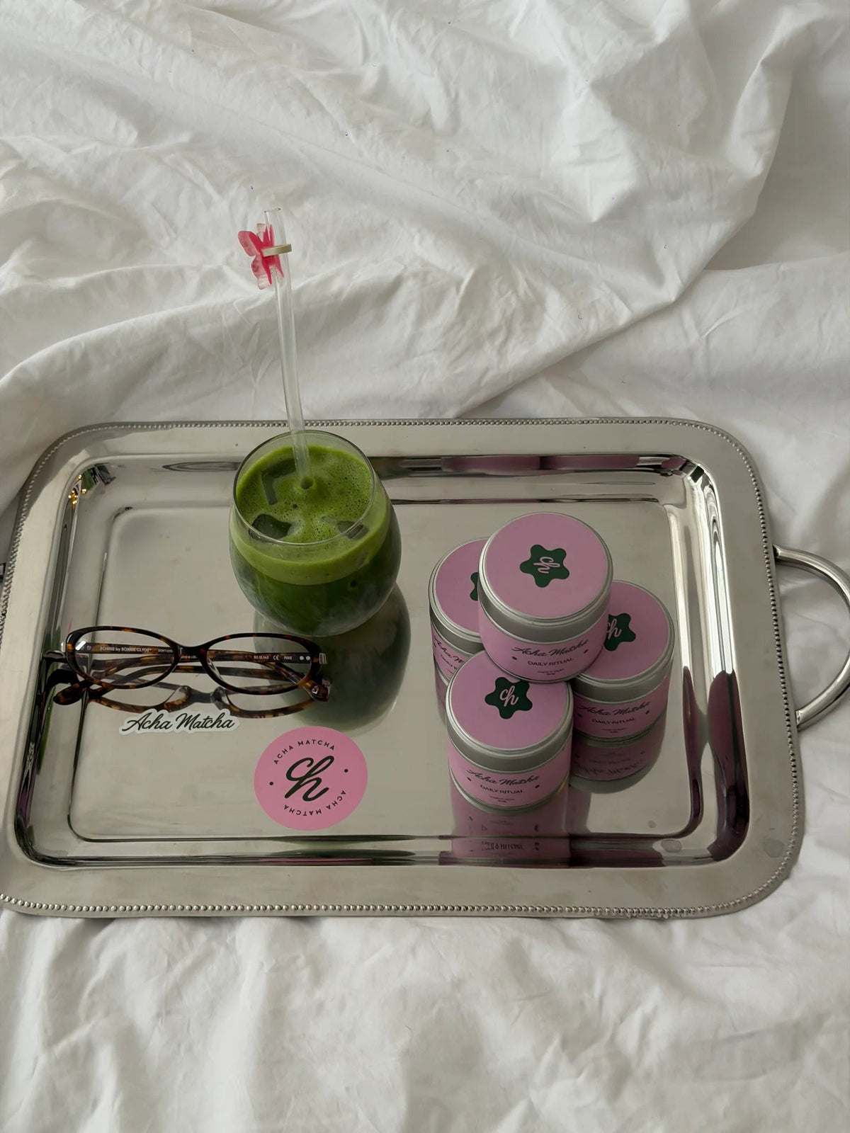 Eisgekühlter Matcha, rosa Dosen und ein Matcha-Besen auf einem Frühstückstablett