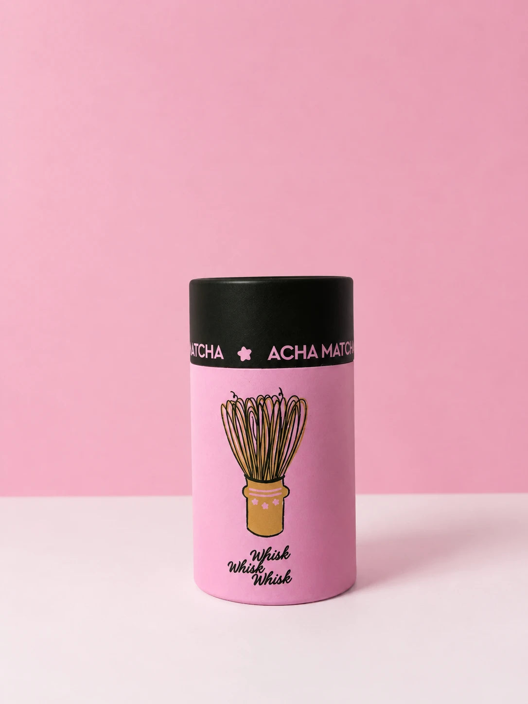 The Whisk in its pink Acha Matcha tube on a pink studio background