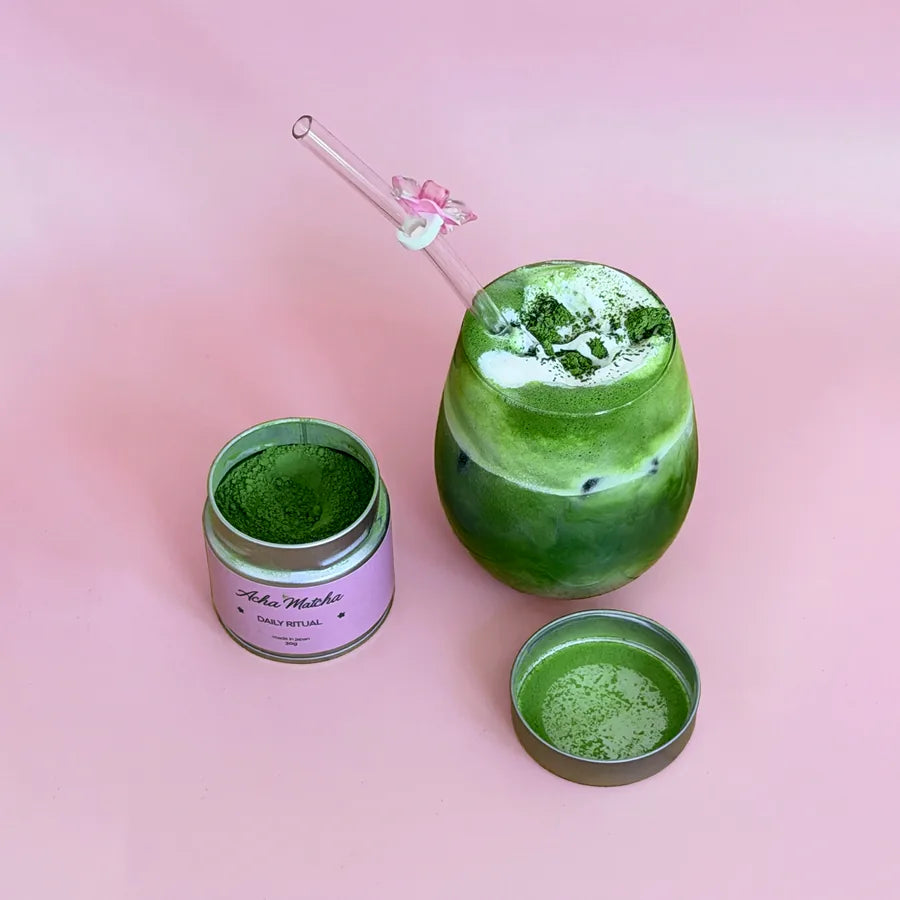 A finished iced matcha beside an open Daily Ritual tin on pink