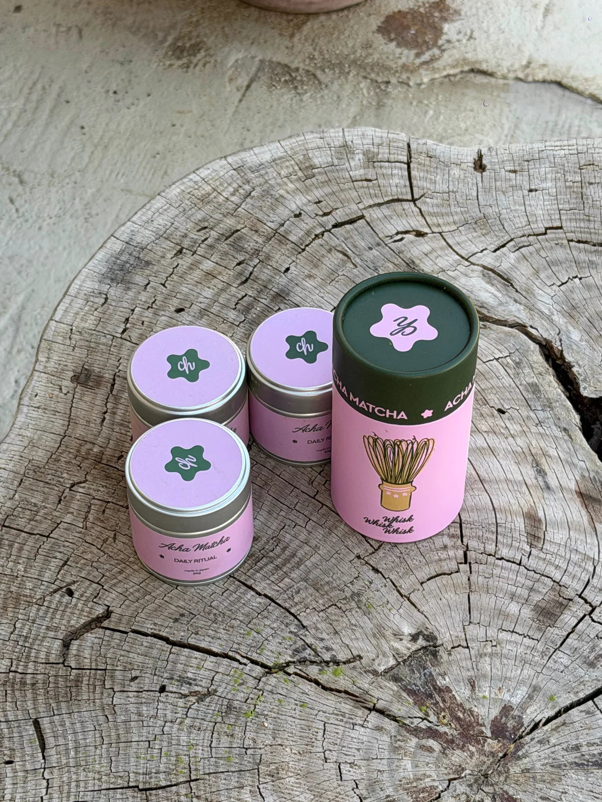 Three pink Acha Matcha tins arranged on natural wood